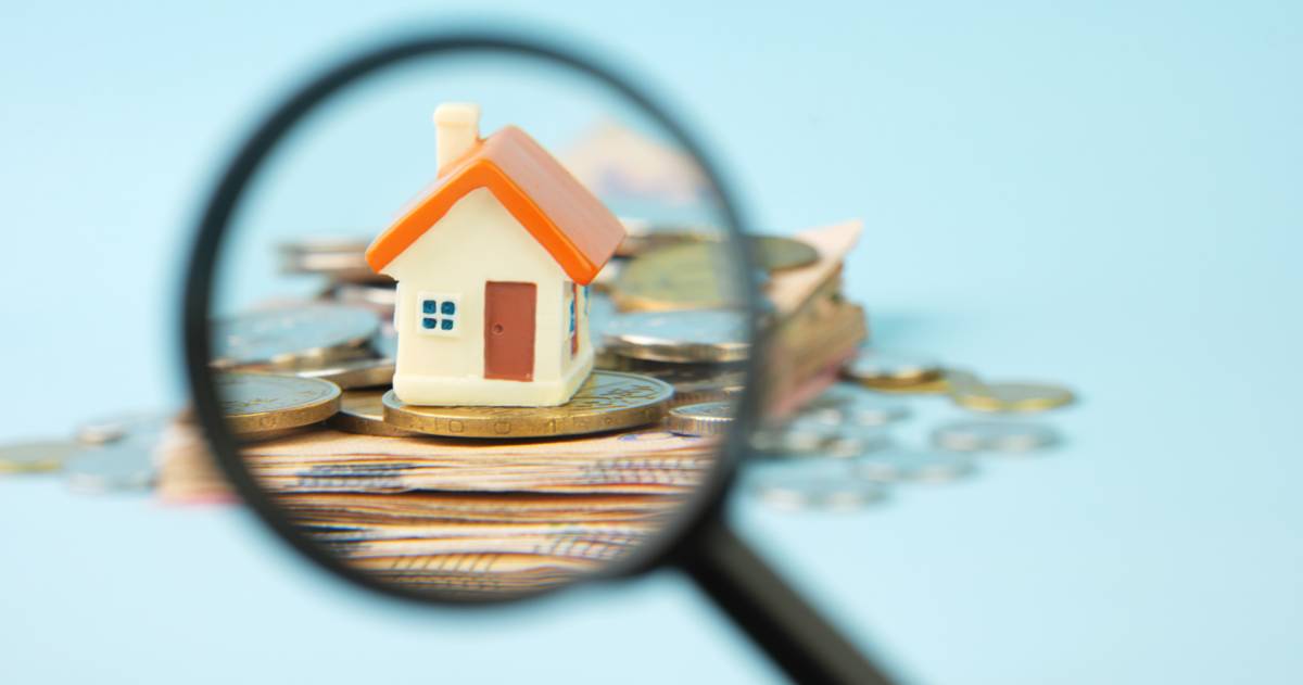 Miniatuur huisje op een stapel met brief- en muntgeld dat wordt bekeken met een vergrootglas