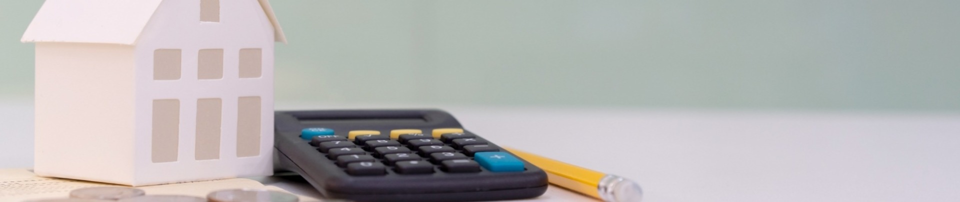 Papieren huis met een rekenmachine, potlood en muntgeld